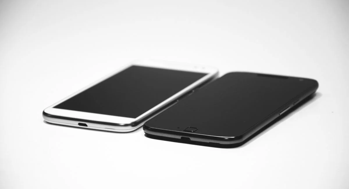 Two smartphones, one black and one white, placed on a white surface, showcasing modern design.
